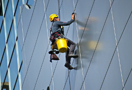 window cleaning worker hanging by ropes as he works on the side of a high-rise building