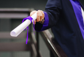 hand of someone in a graduation gown holding out a diploma