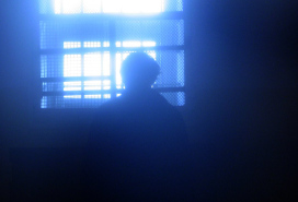 head in silhouette, looking out a prison window from a darkened room