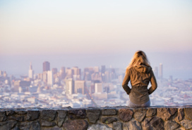 woman sitting on stone wall looking at a city