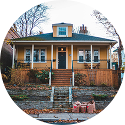 Yellow house with a front porch, white columns, and surrounding trees in a residential neighborhood