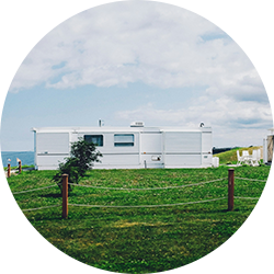 White mobile home and small shed on a grassy lot overlooking the water