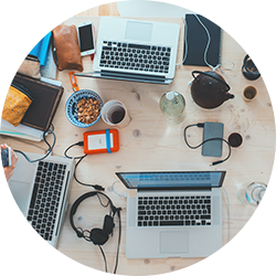 Top view of a desk with laptops, phones, headphones, and office supplies