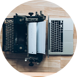 Overhead view of a vintage typewriter placed next to an open laptop on a wooden floor